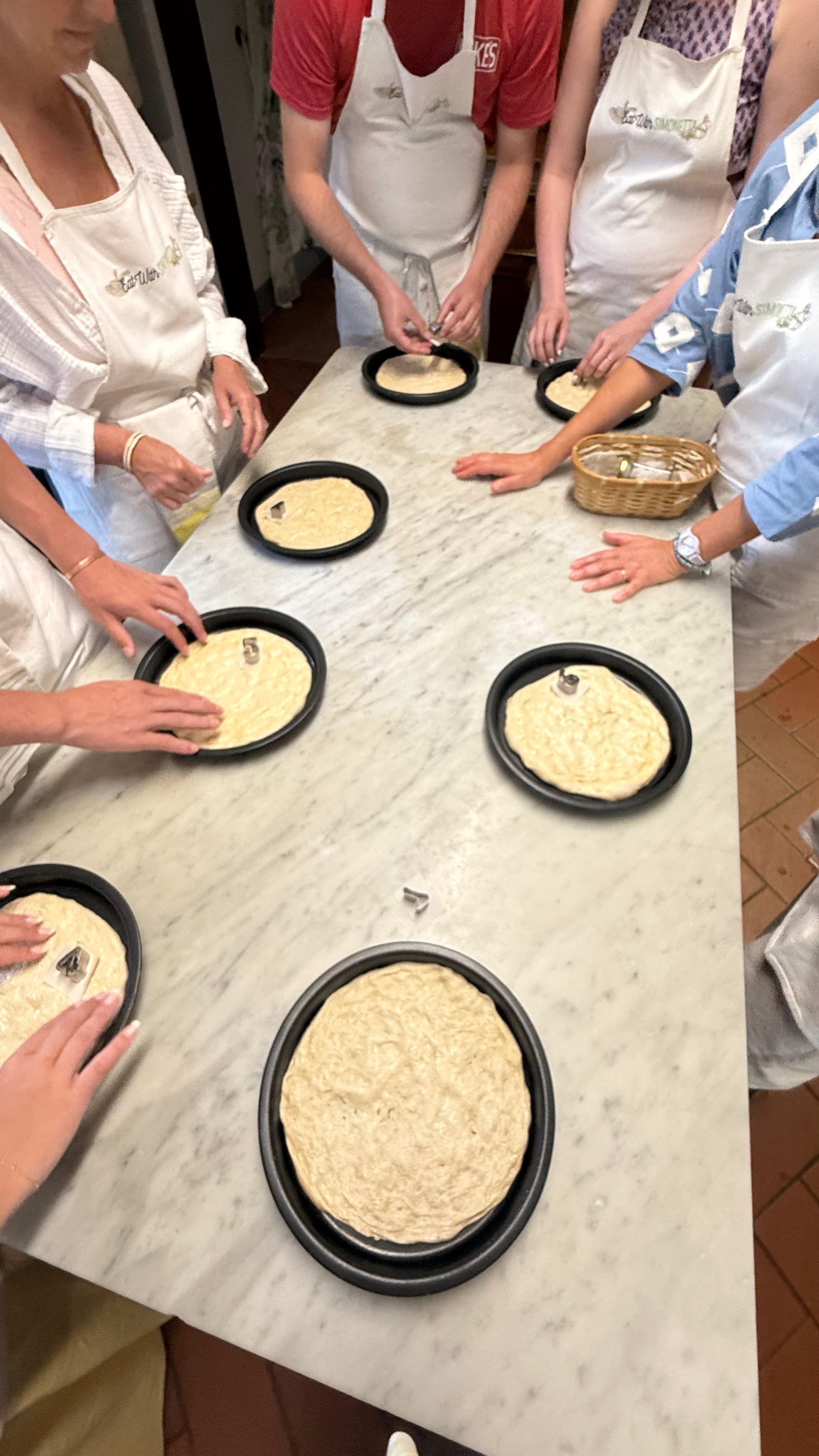 Grupa uczestniczek formująca ciasto na pizzę podczas warsztatów gotowania